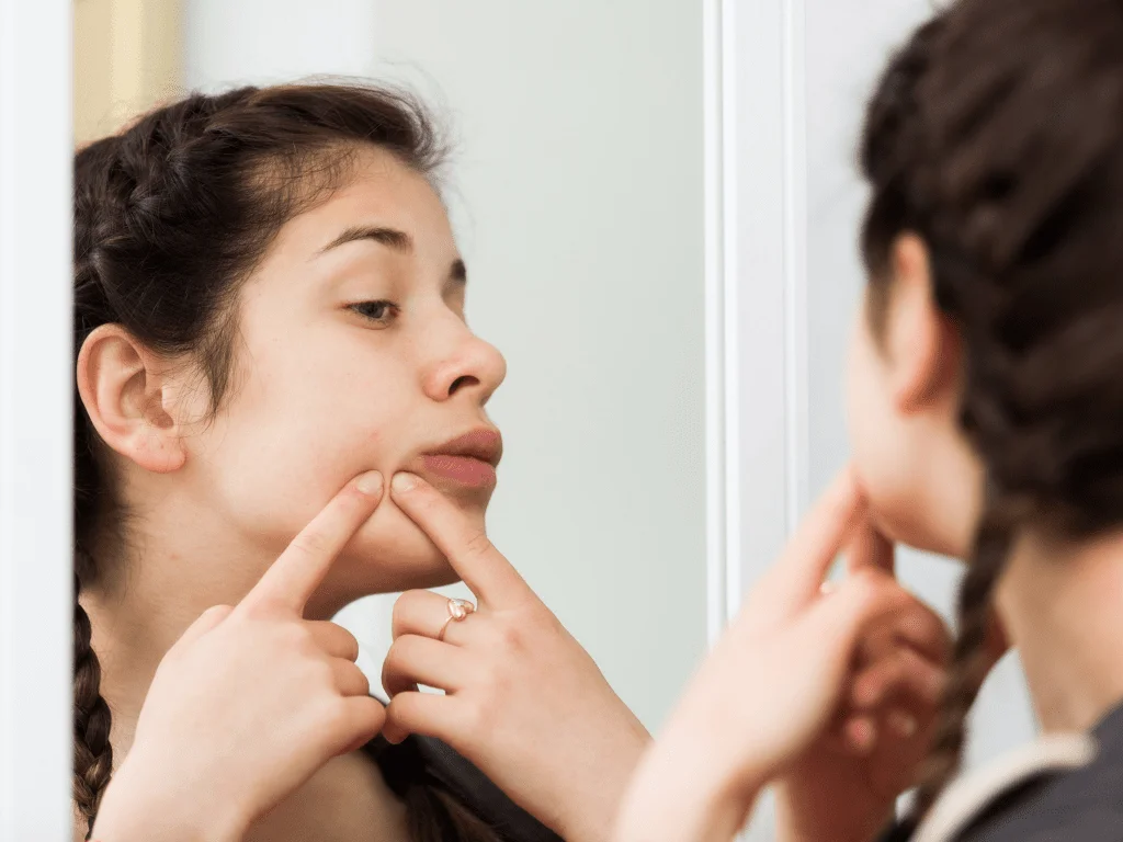 woman popping pimples in front of the mirror