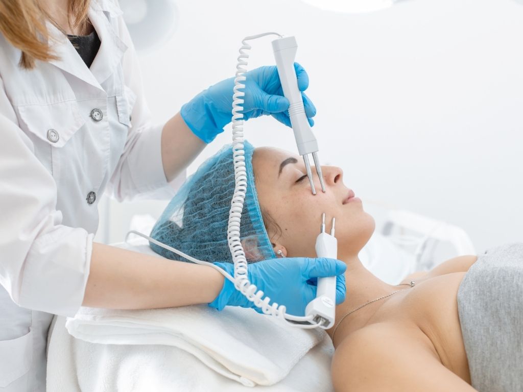 woman with cap on getting a facial treatment with an electrical device