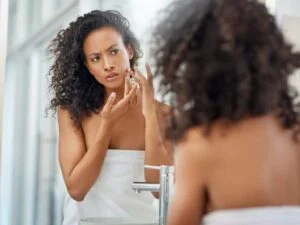black woman in a towel pricking her face